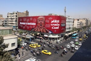 Iraniani in auto davanti a un cartellone anti-Trump a Teheran