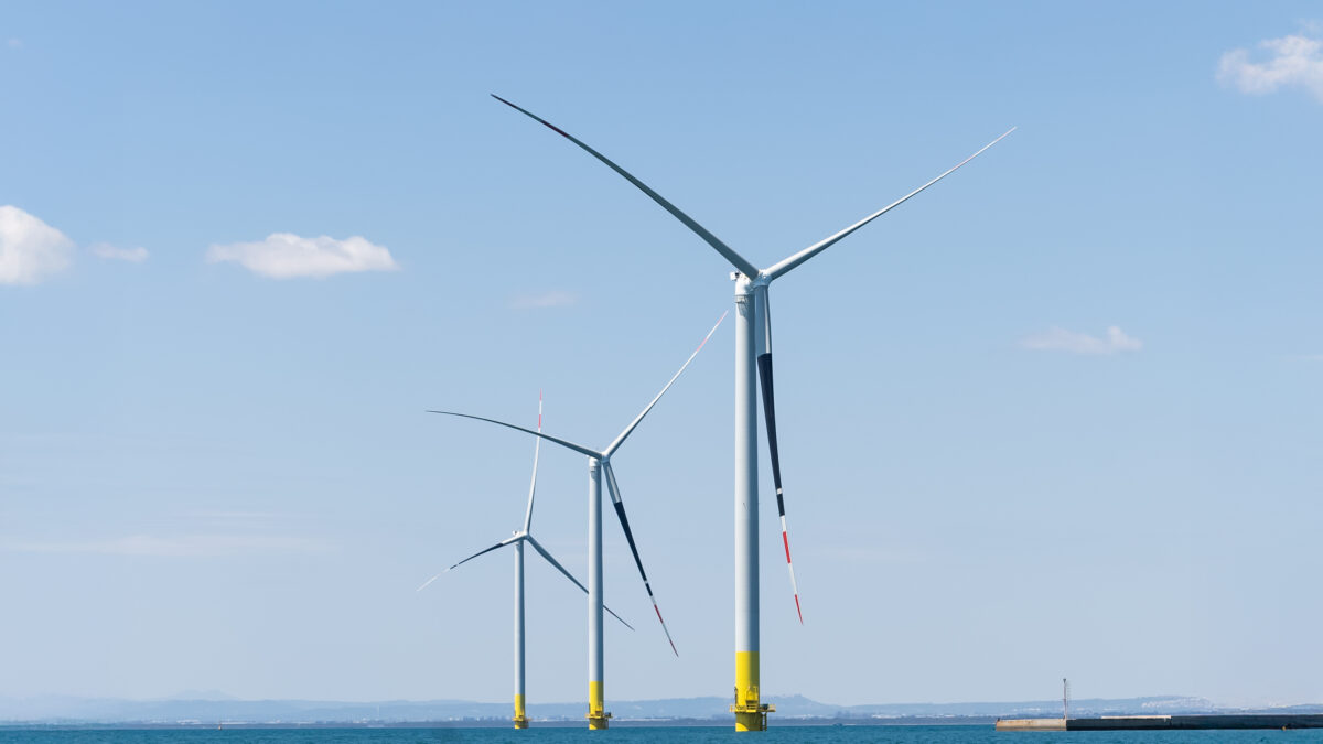 Tre grandi turbine eoliche bianche e gialle svettano nelle acque del mare sotto un cielo azzurro e limpido