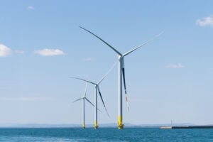 Tre grandi turbine eoliche bianche e gialle svettano nelle acque del mare sotto un cielo azzurro e limpido