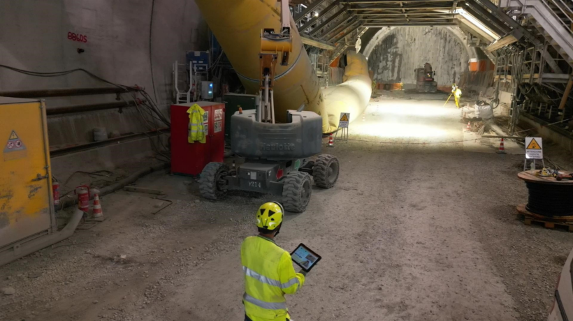 Ingegnere di cantiere visto di spalle con elmetto giallo e gilet ad alta visibilità mentre utilizza un tablet in una galleria sotterranea in lavorazione