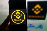 Un utente consulta il sito web di Binance al computer e il logo della piattaforma sullo smartphone