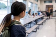 Una bambina in piedi osserva i compagni seduti a mangiare nella mensa scolastica